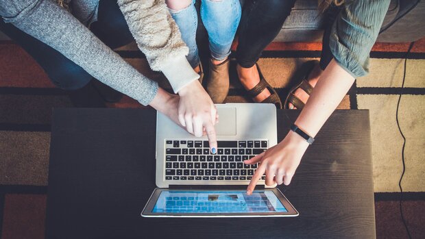  Kolleginnen und Kollegen bedienen zusammen eine Laptoptastatur als Symbol für "Gemeinsam" 